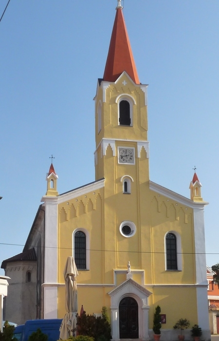 La foto è verticale e mostra la facciata della chiesa di San Zenone. La chiesa è gialla, mentre il campanile ristrutturato è di colore arancione.