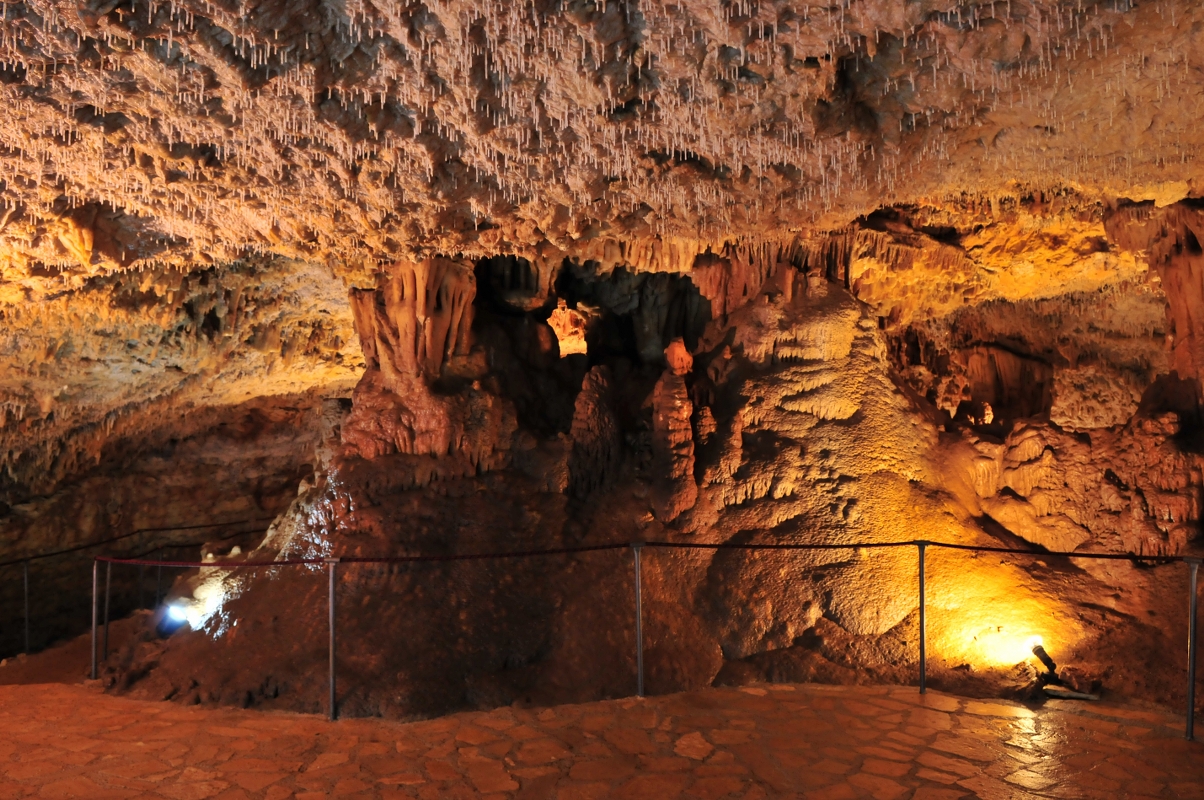 Na slici se vidi unutrašnjost špilje Mramornice, osvijetljena lampama koje stoje na podu. Cijela je slika žućkasto-narančaste boje.